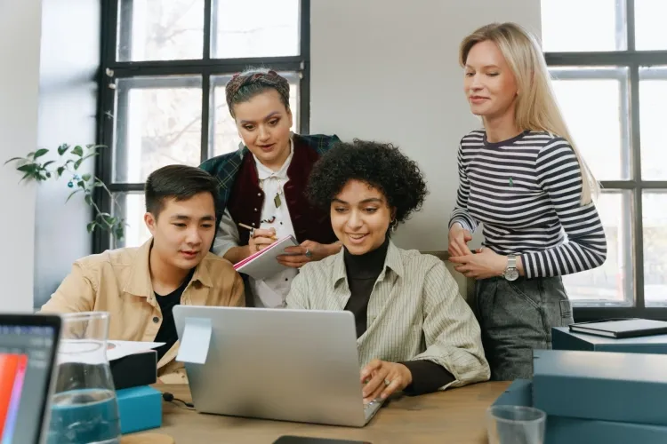 Vier Personen, die um ein Notebook in der Arbeit herumsitzen und an etwas arbeiten
